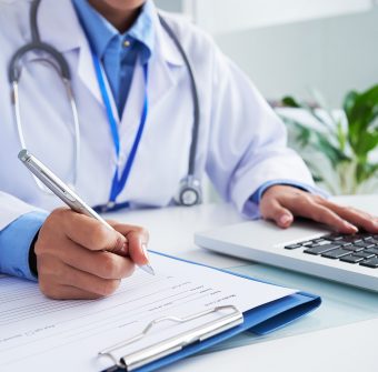 Doctor checking information in computer program before filling medical card